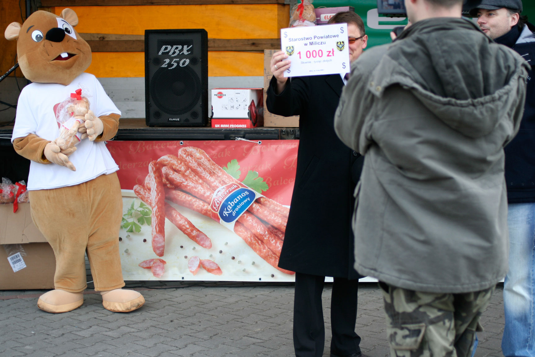 Na fotografii widnieje strój reklamowy w postaci chomika pozujący do zdjęcia na jednej z imprez promocyjnych